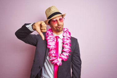 Takım elbiseli genç işadamı şapka gözlüğü takıyor. Havai zambağı, izole edilmiş pembe arka plan, kızgın yüz, negatif işaret baş parmaklar aşağı, reddedilme konsepti.