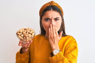 Fıstıklı genç bir kadın, izole edilmiş beyaz arka planda duruyor. Ağzı kapalı, elleri utançla kaplı, korkunun ifadesi, sessizlikten korkmak, gizli bir konsept.