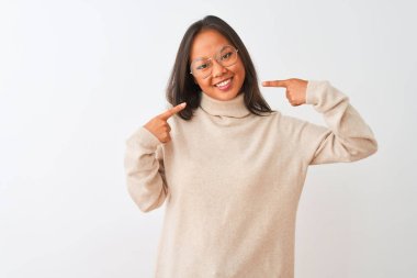 Balıkçı yaka kazak ve gözlük takan genç Çinli kadın izole edilmiş beyaz arka planda gülümseyen ve parmaklarını ve ağzını göstererek gülümsedi. Diş sağlığı konsepti.