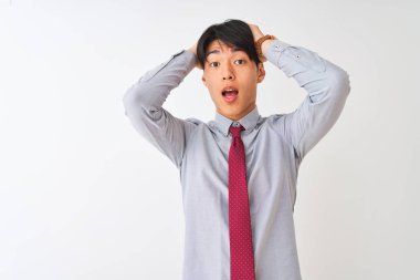 Soyutlanmış beyaz arka planda duran zarif kravat takan Çinli işadamı elleri başında korkmuş, korkmuş ve ağzı açık bir şekilde şok geçirmekten korkmuş.