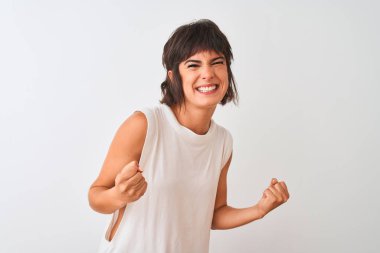 İzole beyaz arka plan üzerinde ayakta rahat t-shirt giyen genç güzel kadın çok mutlu ve heyecanlı silah kaldırdı, gülümseyen ve başarı için çığlık ile kazanan jest yapıyor. Kutlama konsepti.