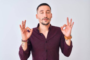 Tecrit edilmiş arka planda duran genç yakışıklı iş adamı rahatla ve gözün kapalı gülümse parmaklarınla meditasyon hareketi yap. Yoga konsepti.