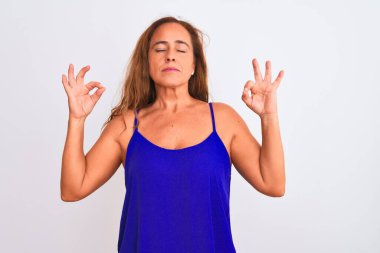 Orta yaşlı olgun bir kadın beyaz soyutlanmış arka planda duruyor rahatlayıp gülümsüyor parmaklarıyla meditasyon hareketi yapıyor. Yoga konsepti.