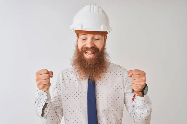 Young redhead irish architect man wearing security helmet over isolated white background excited for success with arms raised and eyes closed celebrating victory smiling. Winner concept.