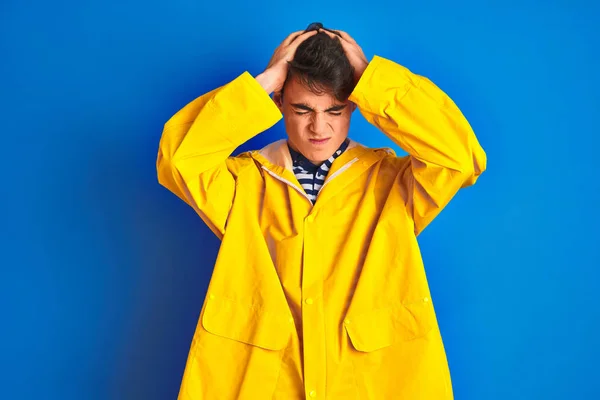 Teenager fisherman boy wearing yellow raincoat over isolated background suffering from headache desperate and stressed because pain and migraine. Hands on head.