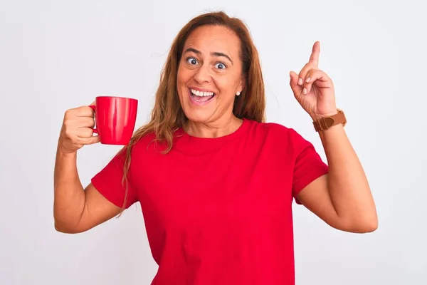 中年熟女飲むの上のホットコーヒーのカップの隔離された背景驚きでアイデアや質問指差し指で幸せな顔 ナンバーワン — ストック写真