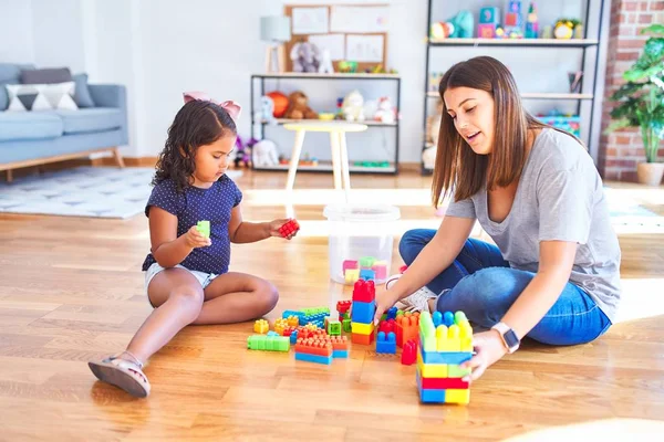 Güzel öğretmen ve küçük kız anaokulunda inşaat bloklarıyla oynuyorlar.