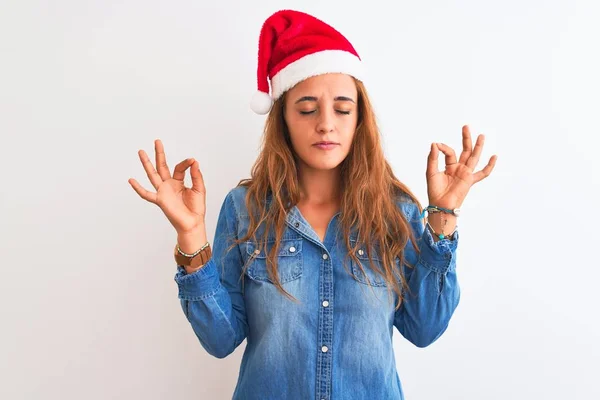 孤立した背景の上にクリスマスの帽子を身に着けている若い美しい赤毛の女性はリラックスし 指で瞑想のジェスチャーをして閉じ目で笑顔 ヨガのコンセプト — ストック写真