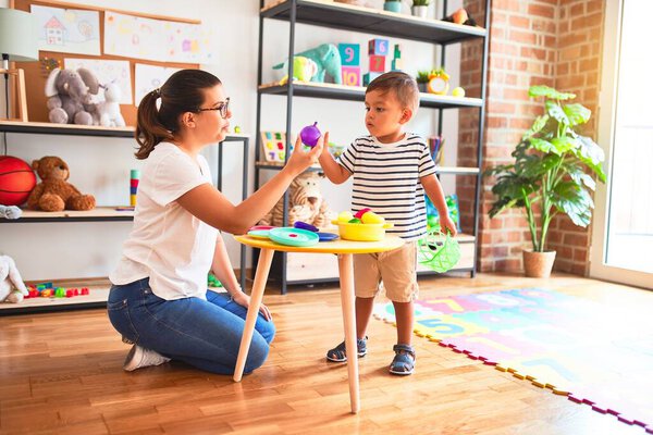 Beautiful toddler boy sitting on puzzle playing with plastic plates, fruits and vegetables at kindergarten