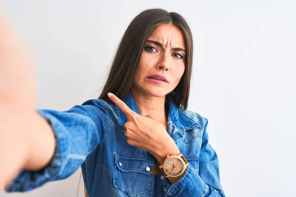 Beautiful woman wearing denim shirt make selfie by camera over isolated white background Pointing aside worried and nervous with forefinger, concerned and surprised expression