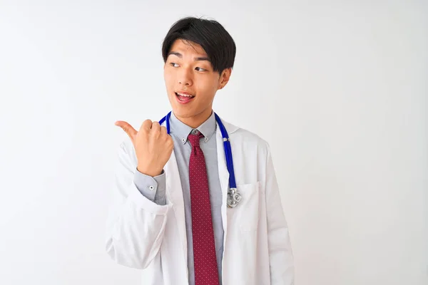 中国医生 戴着外套领带和听诊器 站在与世隔绝的白色背景上 笑容满面 高高兴兴地朝旁边看去 竖起大拇指指指点点 — 图库照片