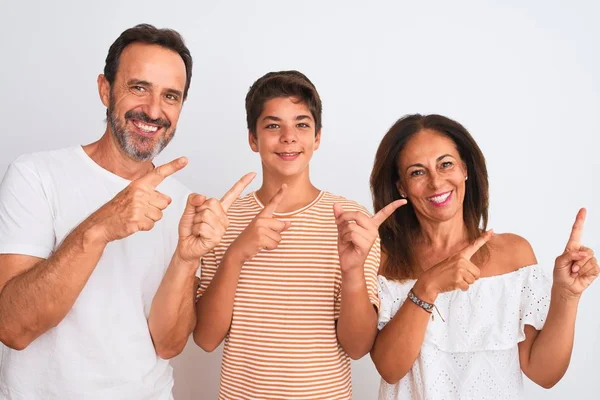 Family of three, mother, father and son standing over white isolated background smiling and looking at the camera pointing with two hands and fingers to the side.