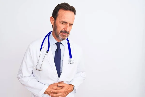 Middle age doctor man wearing coat and stethoscope standing over isolated white background with hand on stomach because indigestion, painful illness feeling unwell. Ache concept.