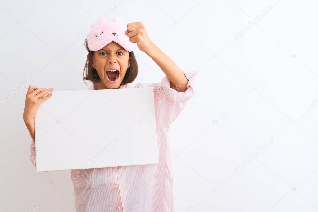 Child girl wearing sleep mask and pajama holding banner over isolated white background annoyed and frustrated shouting with anger, crazy and yelling with raised hand, anger concept