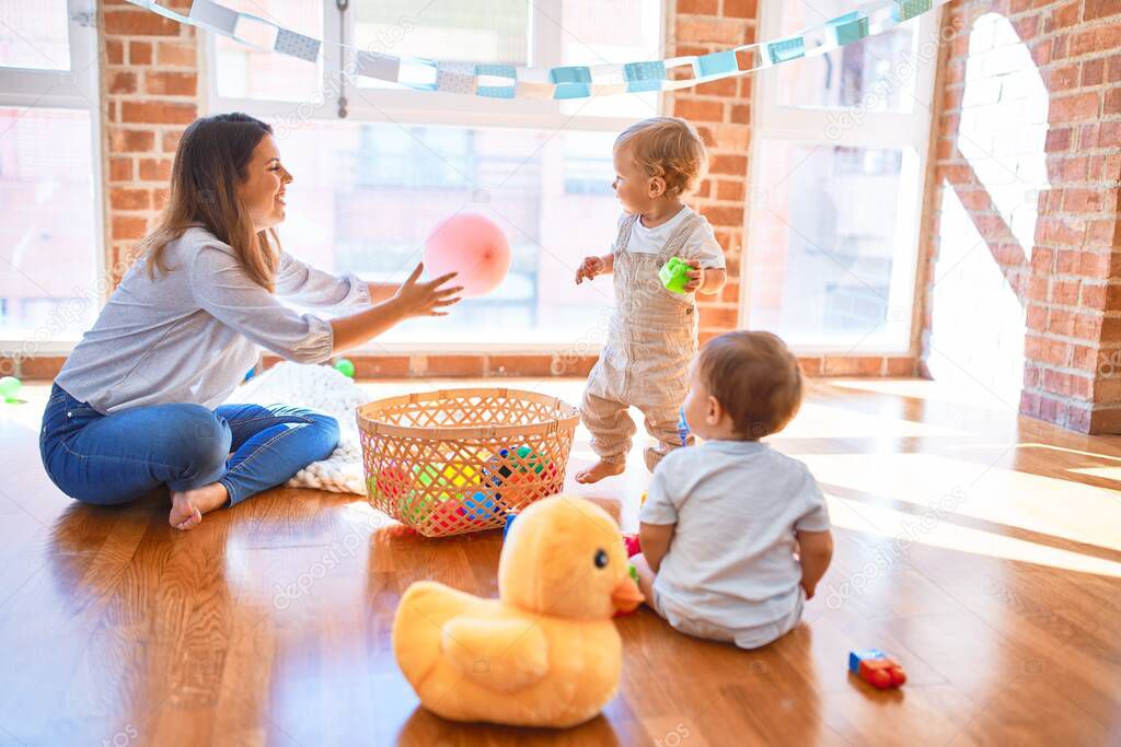 Beautiful teacher and toddlers playing around lots of toys at kindergarten