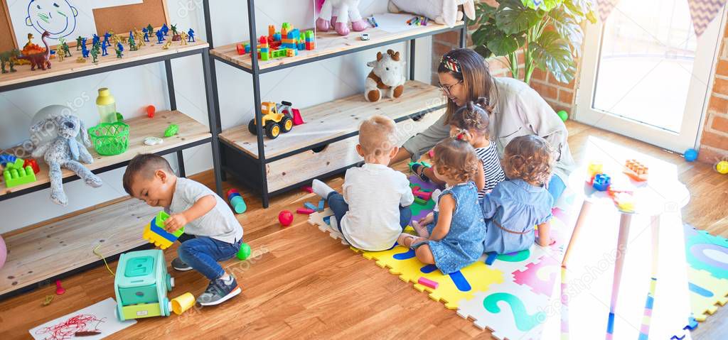 Beautiful teacher and group of toddlers playing around lots of toys at kindergarten