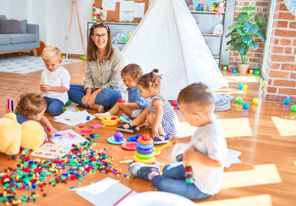 Beautiful teacher and group of toddlers playing around lots of toys at kindergarten