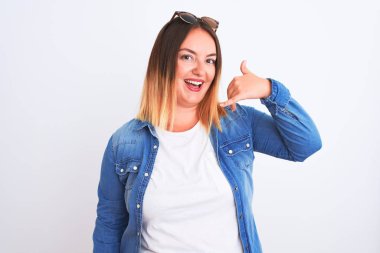 Güzel bir kadın kot gömlek giyiyor, beyaz arka plan üzerinde duruyor, gülümsüyor, telefonla el ve parmak hareketleri yapıyor, telefonda konuşuyor gibi. İletişim kavramları.