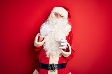 Orta yaşlı yakışıklı bir adam Noel Baba kostümü giyiyor. İzole edilmiş kırmızı arka planda duruyor. İğrenç bir ifade, tiksindirici bir yüz ifadesi var. Eller havada. Can sıkıcı bir kavram..