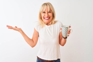 Orta yaşlı bir kadın, izole edilmiş beyaz arka planda durup kahve içiyor. Çok mutlu ve heyecanlı. Kazanan ifade zaferi büyük bir gülümsemeyle kutluyor ve ellerini kaldırıyor.