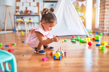 Genç, güzel bir çocuk yerde oturmuş anaokulunda tahta tren oyuncağıyla oynuyor.
