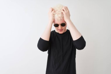 Siyah tişört giyen ve güneş gözlüklü genç albino adam izole edilmiş beyaz arka planda dikiliyor. Ağrı ve migrenden dolayı çaresiz ve stresli. Ellerini başının üstüne koy..