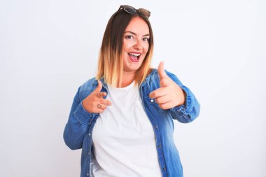 İzole edilmiş beyaz arka plan üzerinde kot gömlek giyen güzel bir kadın mutlu ve komik yüzlü parmaklarını kameraya doğrultuyor. İyi enerji ve titreşimler.