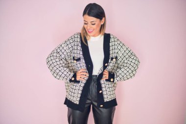 Şık kıyafetler giyen, mutlu ve kendinden emin gülümseyen genç ve güzel bir kadın. İzole edilmiş pembe arka planda yüzünde bir gülümsemeyle duruyorum.