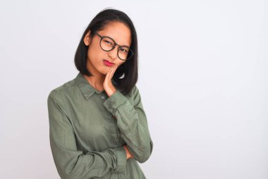 Yeşil gömlek ve gözlük takan Çinli genç bir kadın izole edilmiş beyaz arka plan üzerinde kolları çapraz depresyondan sıkılmış ve yorgun görünüyor..