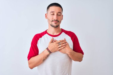 Soyutlanmış arka planda duran yakışıklı genç adam elleri göğsünde, gözleri kapalı ve yüzünde minnet dolu bir jest ile gülümsüyor. Sağlık kavramı.
