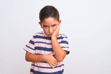 Güzel çocuk, sıradan çizgili tişört giyip izole edilmiş beyaz arka plan üzerinde duruyor. Kollarını kavuşturup depresyondan sıkılmış ve yorgun görünüyor..