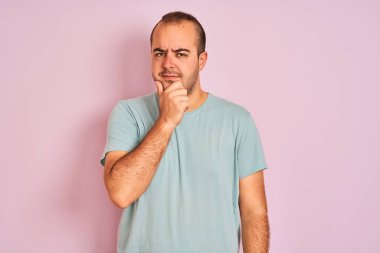 İzole edilmiş pembe arka plan üzerinde duran mavi tişörtlü genç adam kameraya kollarını kavuşturup gülümseyerek ve çenesini kaldırarak bakıyor. Olumlu düşünüyorum..