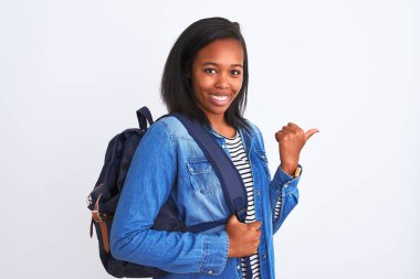Sırt çantası takan genç Afro-Amerikalı bir bayan izole edilmiş arka planı işaret ediyor ve gülümseyen bir yüzle baş parmağıyla gösteriyor.