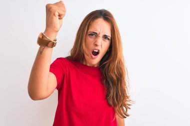 Kızıl saçlı, kırmızı tişörtlü genç bir kadın. İzole edilmiş beyaz bir arka plan üzerinde kızgın ve kızgın. Öfkeyle bağırırken yumruğunu kaldırıyor. Öfke ve agresif kavram.