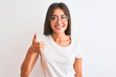 Genç, güzel bir kadın, izole edilmiş beyaz arka planda günlük tişört ve gözlük takıp mutlu bir el hareketi yapıyor. Kameraya bakıp başarıyı gösteren ifade onaylanıyor.