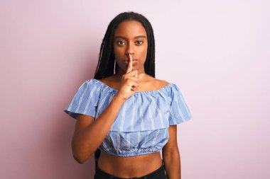Siyah çizgili tişört giyen Afro-Amerikalı bir kadın izole edilmiş pembe arka planda dikilip sessiz olmak istiyor. Sessizlik ve gizli konsept.