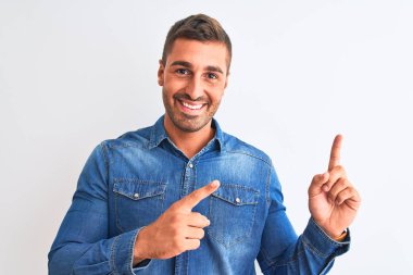 Kot ceket giyen genç yakışıklı arka planda duruyor gülümsüyor ve kameraya bakıyor iki eliyle ve parmaklarıyla kenarı işaret ediyor..