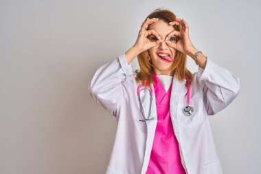 İzole edilmiş arka planda pembe steteskop takan beyaz saçlı doktor kadın dürbünün dili çıkarması, gözlerin parmaklarından içeri bakması gibi iyi hareketler yapıyor. Çılgın ifade.