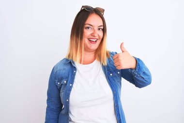 İzole edilmiş beyaz arka plan üzerinde kot gömlek giyen güzel bir kadın mutlu bir el hareketi yapıyor. Kameraya bakıp başarıyı gösteren ifade onaylanıyor.