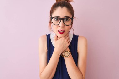 Atkuyruklu, zarif bir elbise ve gözlük takan kızıl saçlı bir kadın izole edilmiş pembe arka planda bağırıyor ve boğuluyor çünkü acı verici bir boğulma var. Sağlık problemi. Boğulma ve intihar konsepti.