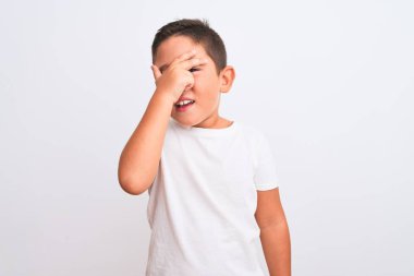 İzole edilmiş beyaz arka plan üzerinde duran sıradan tişört giyen güzel çocuk şok içinde yüzünü ve gözlerini kapayarak utangaç bir ifadeyle parmaklarının arasından bakıyor..