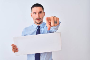 Genç iş adamı arka planda boş bir pankart tutuyor ve kamerayı işaret ediyor. Ve sen, el işareti, ön taraftan pozitif ve kendinden emin bir hareket.