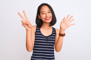 İzole edilmiş beyaz arka plan üzerinde duran çizgili tişört giyen genç Çinli kadın yedinci parmaklarını gösterirken kendinden emin ve mutlu bir şekilde gülümsüyor..