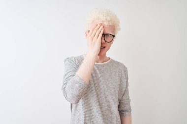 Genç albino sarışın adam çizgili tişört ve gözlük takıyor. İzole edilmiş beyaz arka plan üzerinde. Bir gözünü eliyle kapatıyor..