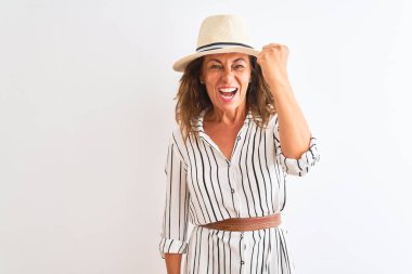 Orta yaşlı iş kadını çizgili elbise ve şapka giyip izole edilmiş beyaz arka plan üzerinde kızgın ve kızgın bir şekilde yumruğunu kaldırırken öfkeyle bağırıyor. Öfke ve agresif kavram.