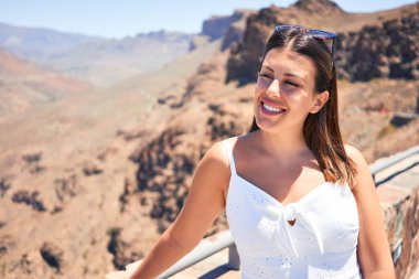 Genç ve güzel bir turist kadın dağ manzarasında mutlu bir şekilde gülümsüyor yaz tatilinin tadını çıkarıyor.