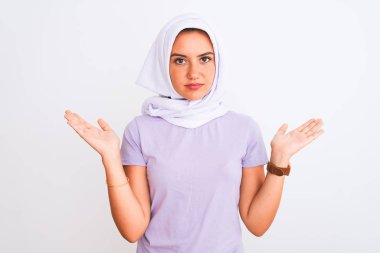 İzole edilmiş beyaz arka plan üzerinde duran tesettürlü genç, güzel bir Arap kız. Kolları ve elleri havada, kafası karışmış bir ifade. Şüphe kavramı.