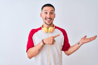 İzole edilmiş arka planda kulaklık takan genç yakışıklı adam kameraya hayret ediyor ve gülümsüyor..