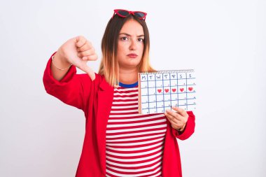 Genç, güzel bir kadının, izole edilmiş beyaz arka plan üzerinde duran, kızgın yüzlü, negatif işaretli, başparmakları aşağıda, reddedilme kavramından hoşlanmadığını gösteren bir takvim.