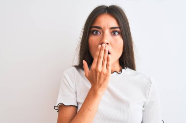 Gündelik tişört giyen genç, güzel bir kadın izole edilmiş beyaz arka planda duruyor. Ağzı kapalı, elleri utançla kaplı, hata yüzünden şoka uğramış, korku ifadesi, sessizlikten korkmak, gizli konsept.